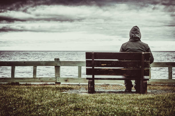 man sitting on bench overlooking sea - loneliness solitude sadness depression imagens e fotografias de stock