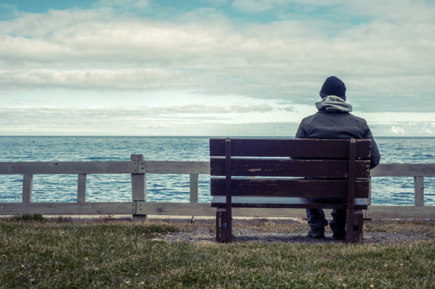 istock Man sitting on bench overlooking sea 830661082