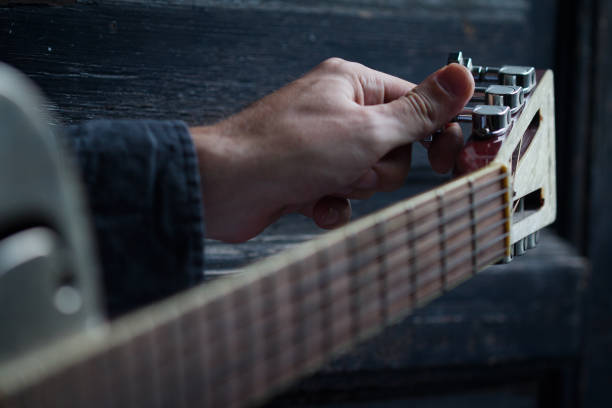 tuning an acoustic guitar on dark background stock photo