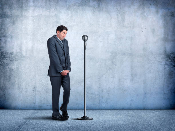 Businessman With Fear Of Public Speaking A businessman sheepishly steps up to a microphone as he is exhibits his fear of public speaking. shy stock pictures, royalty-free photos & images