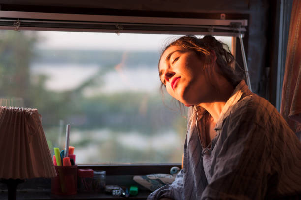 young woman enjoying morning sun next to her window stock photo