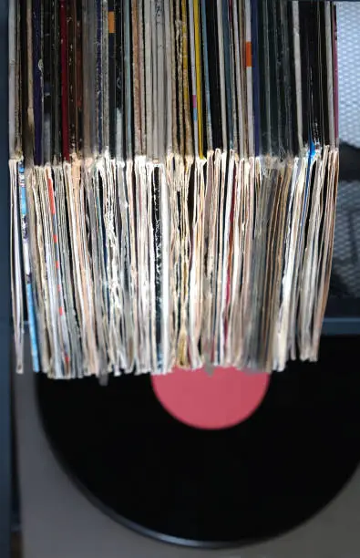 Pile of many close standing vinyl records in old covers and turntable in gray case on a desk top view