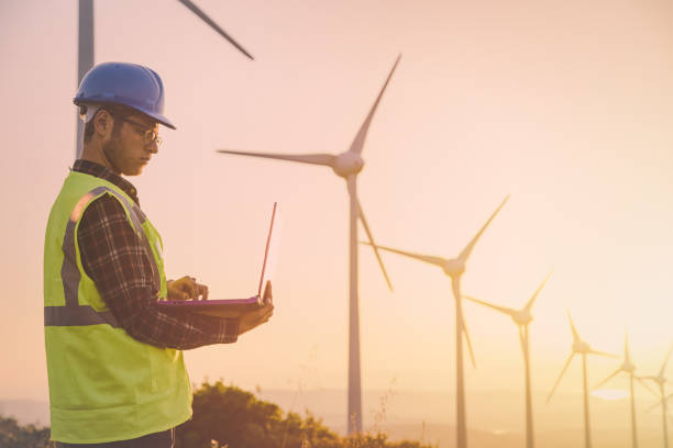 istock Young maintanence engineer using computer in wind turbine farm at sunset 830764364