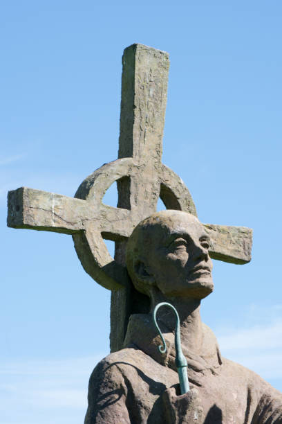 istock A saint statue holding a staff with a cross and blue sky background 830765630
