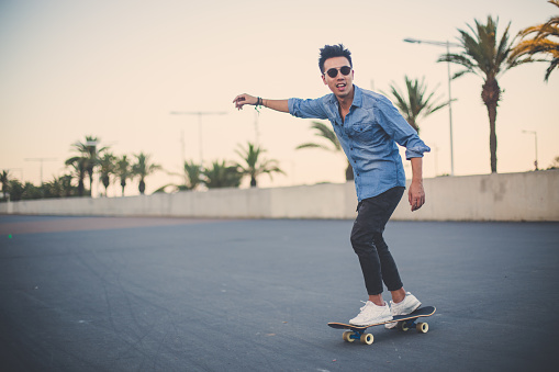 front view of a handsome caribbean man looking at the camera with one foot in his skateboard