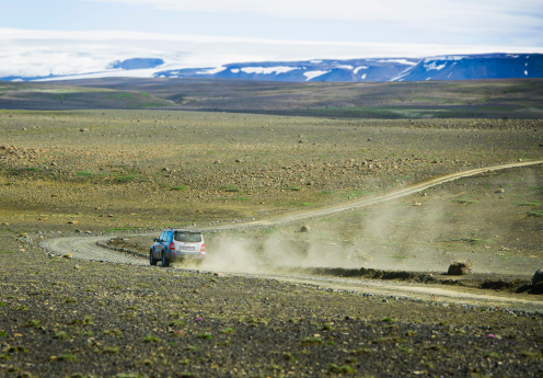 Rear view of an SUV making dust tracks on a barren dirt road in Kerlingarfj?ll mountain range near Reykjavik, Iceland. The mountains are volcanically active, with many hot springs, steam vents and geysers visible throughout the range. The Hofsj?kull Glacier is visible in the far background.