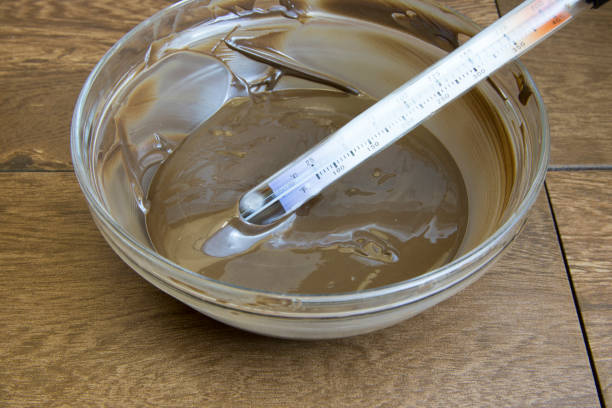 Glass bowl full of tempered dark chocolate with candy thermometer.