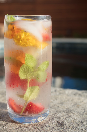 Glass of cold water infused with fruit, mint and edible flowers and ice