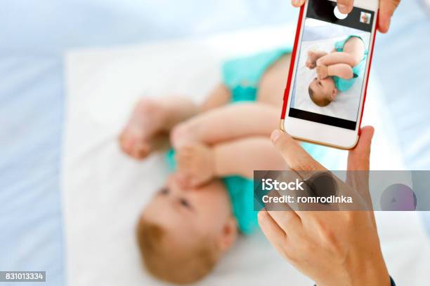Parent Taking Photo Of A Baby With Smartphone Adorable Newborn Child Taking Foot In Mouth Stock Photo - Download Image Now