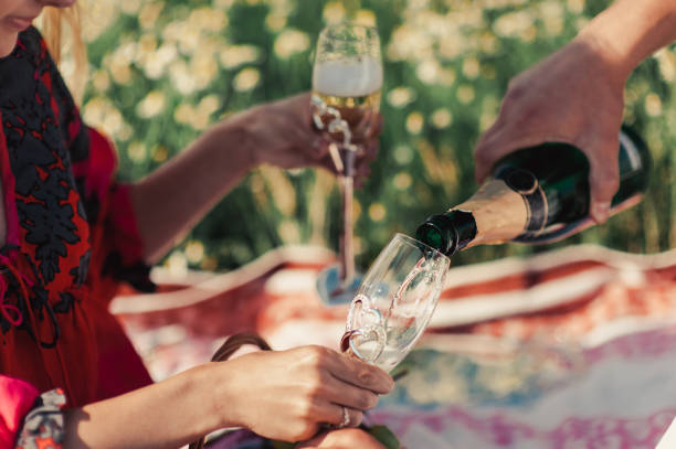 The guy pours champagne in a glass at a picnic