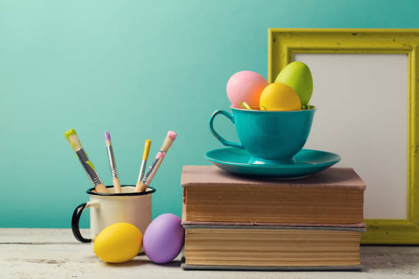 istock Easter holiday celebration with handmade painted eggs in coffee cup, books and brushes. Creative workplace concept 831046634