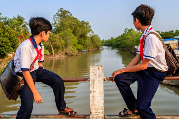 istock Two Vietnamese schoolboys sitting on a bridge, Mekong River Delta, Vietnam 831089718