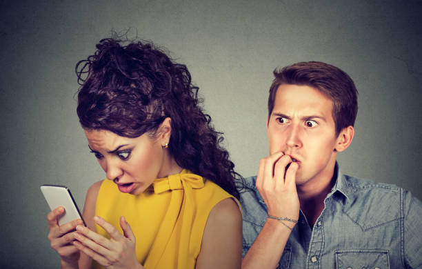 istock A cheating boyfriend. Anxious man nervously biting fingernails while shocked girlfriend reading text messages on his mobile phone 831092464