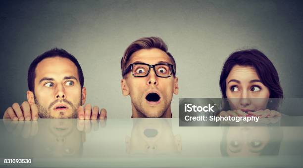 Scared Young People Two Men And A Woman Hiding Peeking Form Under The Table Stock Photo - Download Image Now