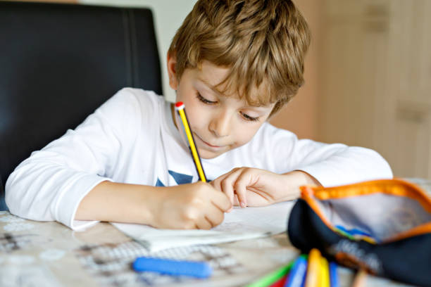 istock Tired kid boy at home making homework writing letters with colorful pens 831096034