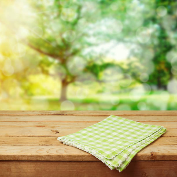 istock Empty wooden deck table with checked tablecloth over green park bokeh background for product montage display 831109542