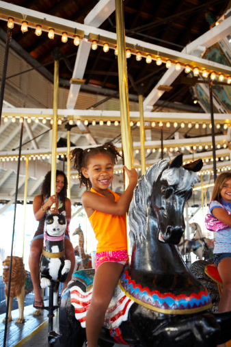 happy baby girl rides a carousel on a horse in an amusement Park in summer