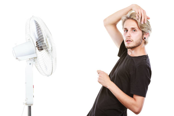 istock Young man fighting with wind from cooling fan 831163084