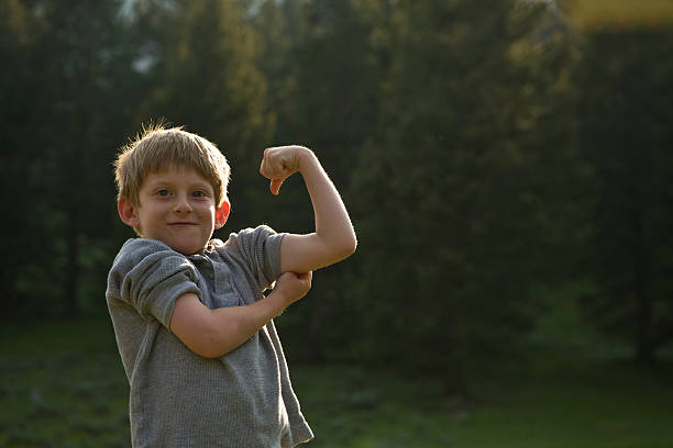 boy flexes his muscles in wilderness on camp trip. - flexing muscles child little boys bicep foto e immagini stock