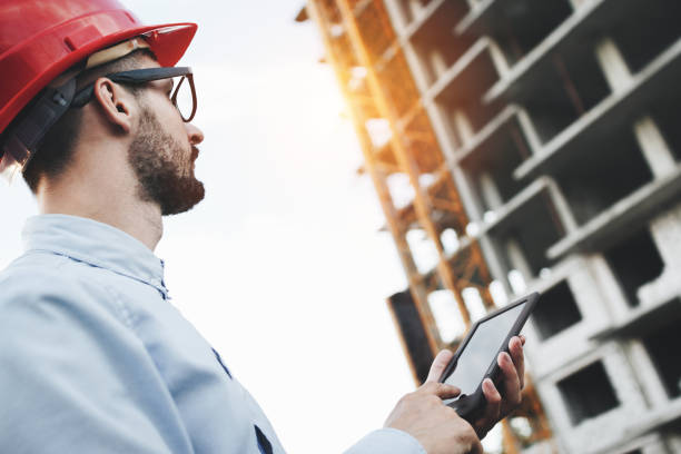 istock Young bearded businessman builder with modern electronic tablet on construction site. Architect looks at industrial construction of plant 831213272
