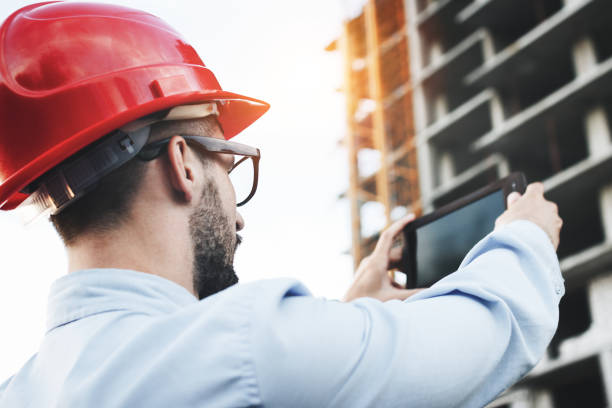 istock Engineer inspector for construction of industrial facilities works on construction site. Portrait of modern architect holding electronic tablet on background of building being built. oncept of modern engineer of builder and industry 831213292