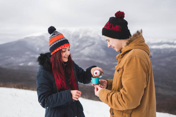 couple drink hot tea from thermos at winter. mountains in snow at background - sexual issues sexual activity couple tan imagens e fotografias de stock