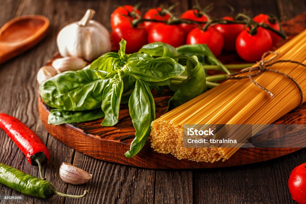 Products for cooking - pasta, tomatoes, garlic, pepper, and basil Products for cooking - pasta, tomatoes, garlic, pepper, and basil on the old wooden background. Healthy Eating Stock Photo