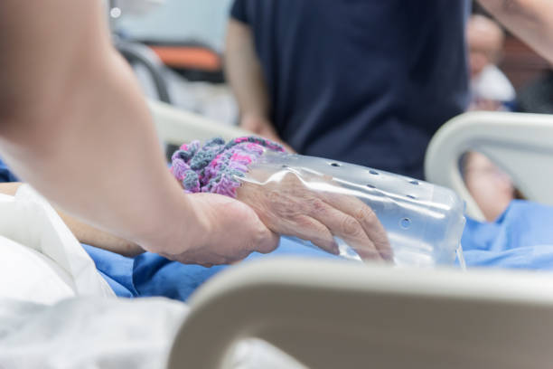 Patient in the hospital with saline intravenous and relatives patient hand holding a elderly patient hand with DIY restraint gloves stock photo