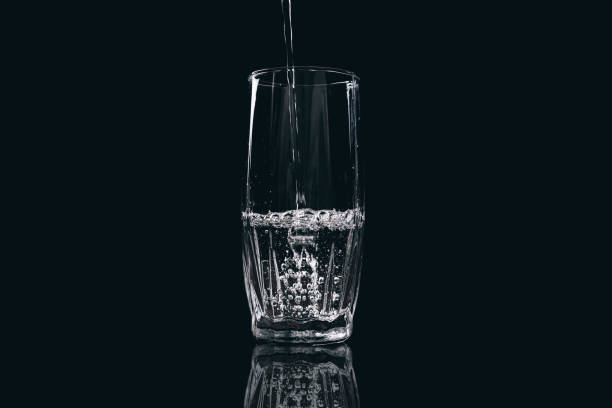 istock Water is poured into a glass on a black background 831314904