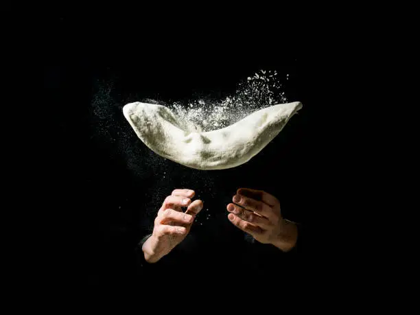 Fliying pizza dough with flour, on drak background
