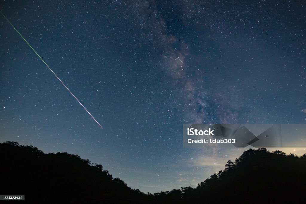 A meteor shoots across the night sky sky leaving a trail of light across the milky way Meteor Stock Photo