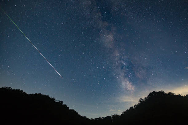 A meteor shoots across the night sky sky leaving a trail of light across the milky way stock photo