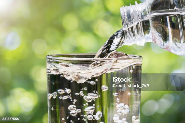 Foto de Closeup De Água Que Flui Da Garrafa De Água Potável Em Vidro Em Fundo De Bokeh Turva Natureza Verde Saudável Beber O Conceito De Água Limpa e mais fotos de stock de Água