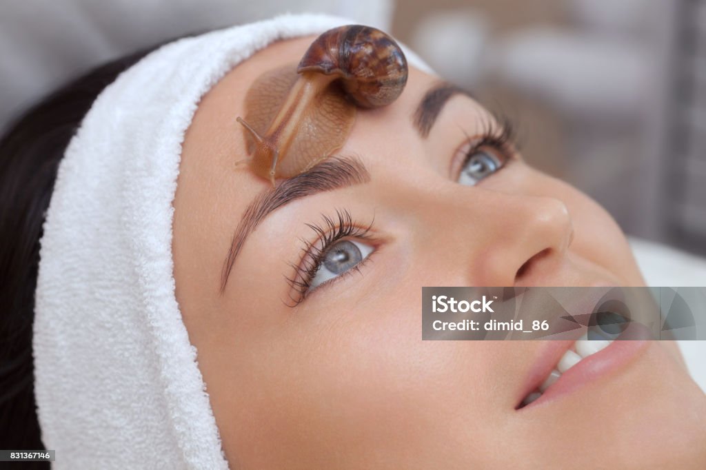 Cosmetological procedure. Beautiful young woman with a snail ahatin on her face Cosmetological procedure. Beautiful young woman with a snail ahatin on her face in a beauty salon. Snail Stock Photo