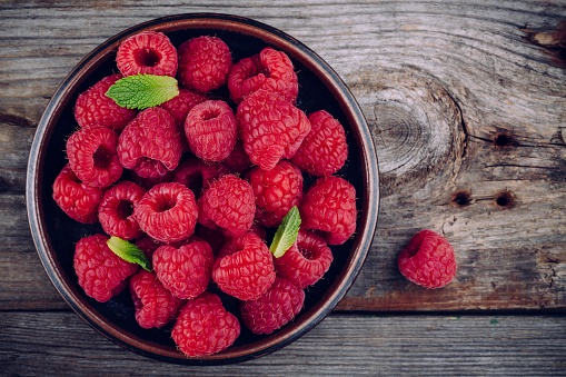 Fresh ripe organic raspberries in a plate on a wooden background