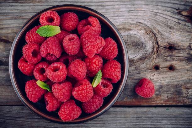 Fresh ripe organic raspberry in a plate on a wooden background Fresh ripe organic raspberries in a plate on a wooden background raspberry stock pictures, royalty-free photos & images