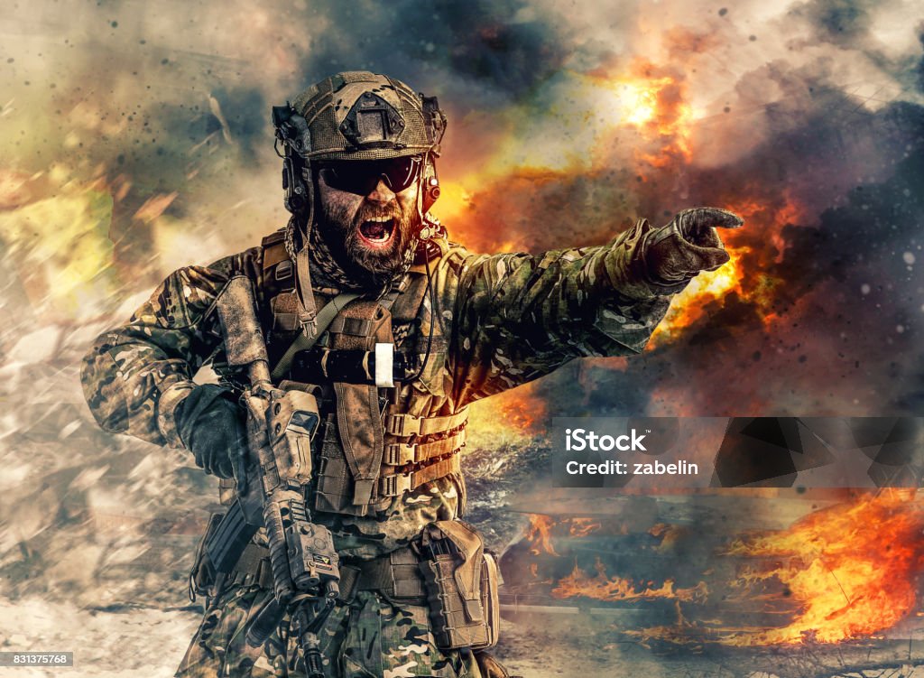 special forces in action Bearded soldier of special forces in action pointing target and giving attack direction. Burnt ruins, Heavy explosions, gunfire and smoke billowing on background Armed Forces Stock Photo