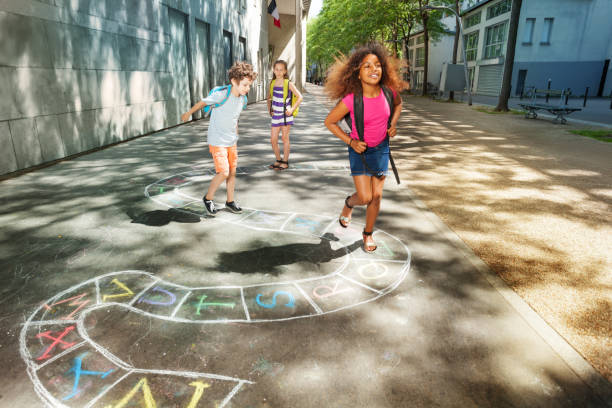Three happy school age kids play hopscotch