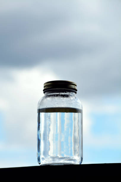 istock Glass Jar Filled with Rainwater with Rain Clouds in the Background 831390182