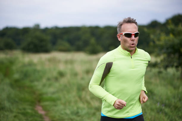 Healthy fit man wearing sunglasses jogging through rural grassland on a country track with copy space behind him on a blurred background in a close up upper body view