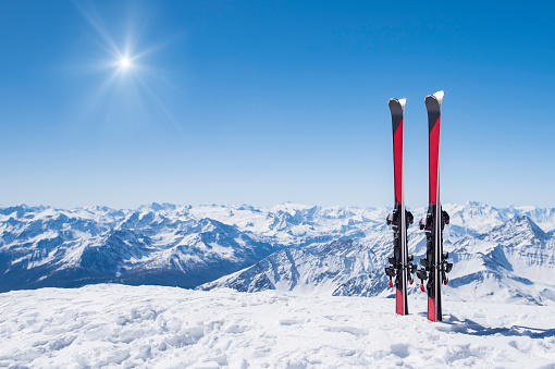 Pair of skis in snow with copy space. Red skis standing in snow with winter mountains in background. Winter holiday vacation and skiing concept.