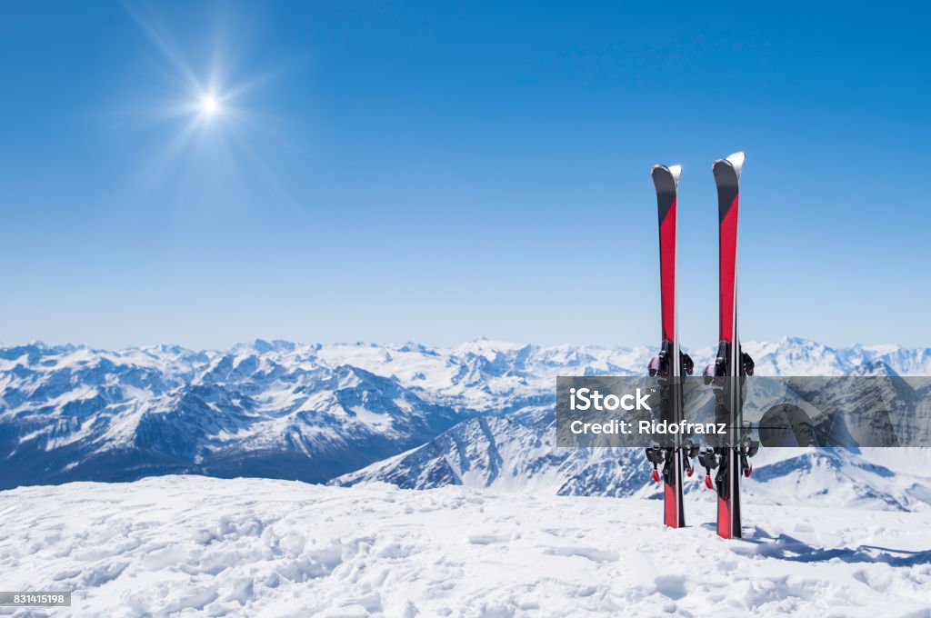 Winter holiday landscape Pair of skis in snow with copy space. Red skis standing in snow with winter mountains in background. Winter holiday vacation and skiing concept. Skiing Stock Photo