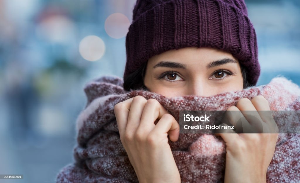 Woman feeling cold in winter Winter portrait of young beautiful woman covering face with woolen scarf. Closeup of happy girl feeling cold outdoor in the city. Young woman holding scarf and looking at camera."r Winter Stock Photo