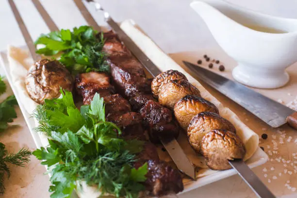 Shish-kebab with grilled vegetables on white dish. Meat, field mushrooms and fresh green parsley, barbecue and natural food preparing in restaurant