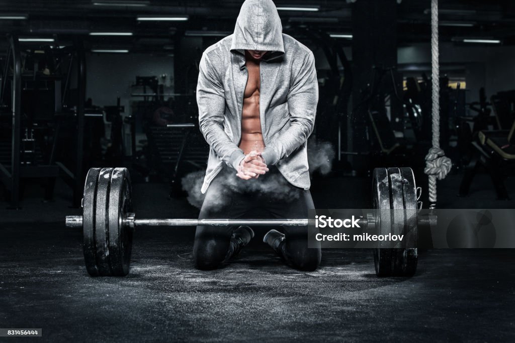 Muscular young fitness sports man workout with barbell in fitness gym Athletic shirtless young sports man - fitness model with barbell in gym. Body Building Stock Photo