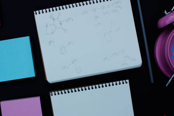 istock Pink alarm clock, stickers, open notepad with white space for text, written chemical formulas, pencil. School supplies on blackboard or chalkboard black background. 831456748