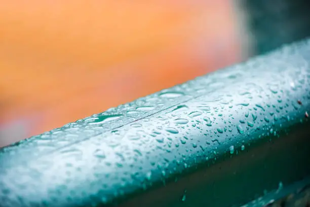 Water drops on metal railing during heavy rain with colorful paint