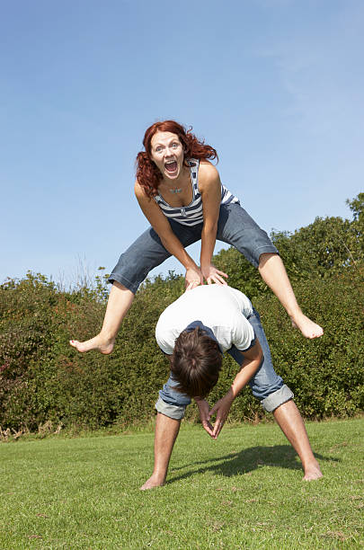 portrait of woman jumping over the top of man - leapfrog - fotografias e filmes do acervo