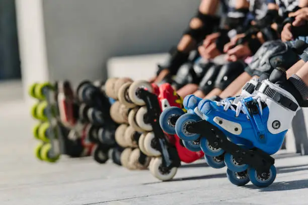 Photo of Feet of rollerbladers wearing inline roller skates sitting in outdoor skate park, Close up view of wheels befor skating