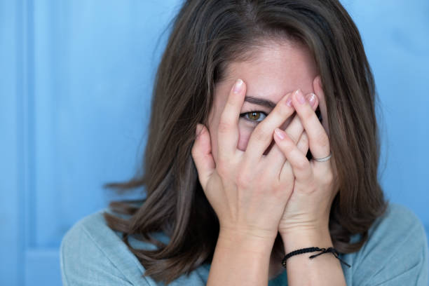 Studio shot of brunette girl hiding eyes under hand while feeling ashamed. Studio shot of brunette girl hiding eyes under hand while feeling ashamed. Caucasian young woman in white shirt covering face with hand. Human facial expressions and emotions shy stock pictures, royalty-free photos & images